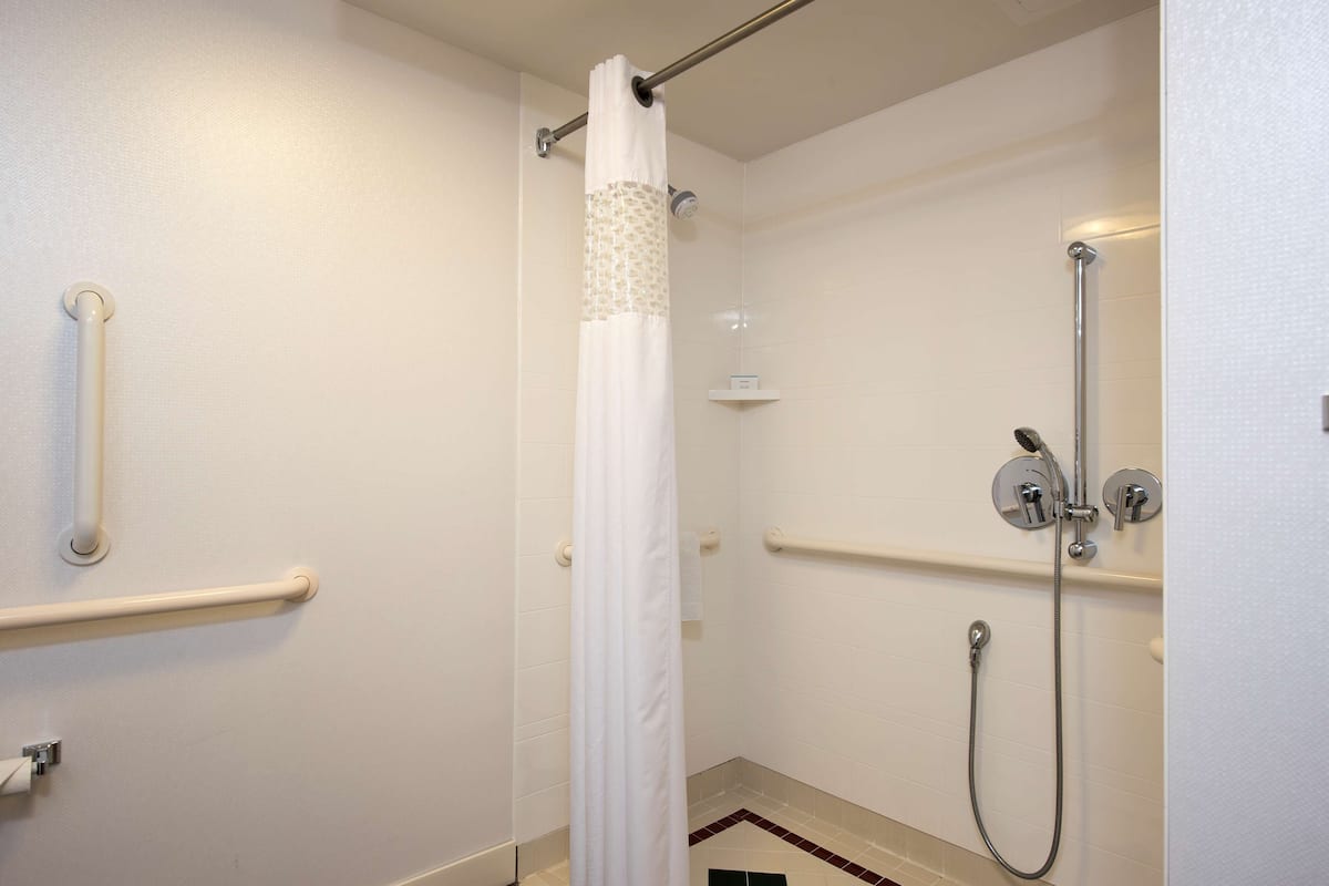 A shower area with a white curtain, grab bars, and a handheld showerhead.