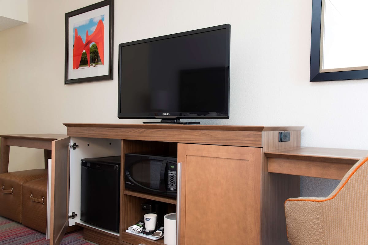 Ein kleines Hotelzimmer mit Flachbildfernseher an einem Holzkasten, einer Mikrowelle und einer kleinen Kaffeemaschine.