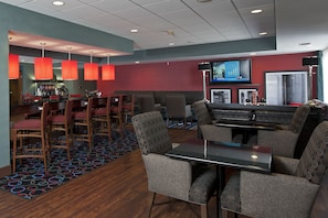 A hotel lobby with a bar area, seating arrangements, and a television screen. - Hampton Inn Grand Rapids-South (Wyoming)
