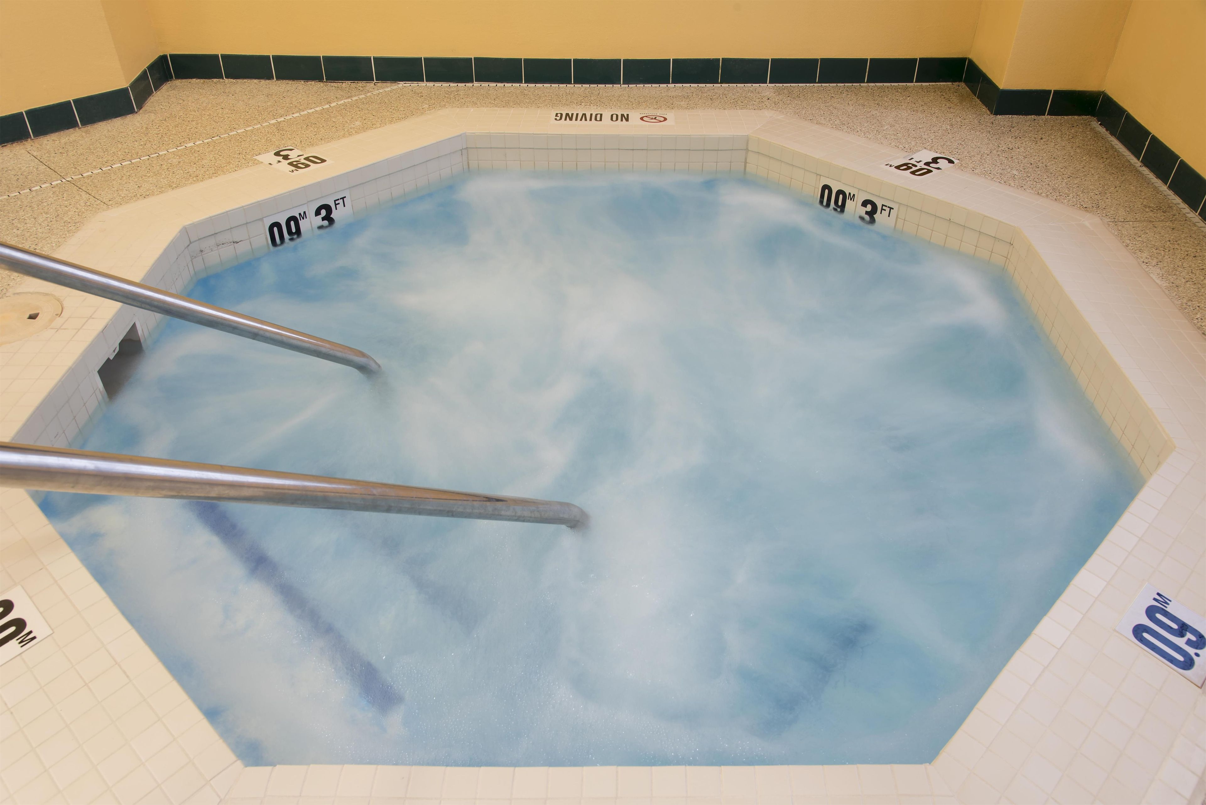 Un jacuzzi con interior de azulejos, barandales de metal y marcas de profundidad que indican 3 pies.