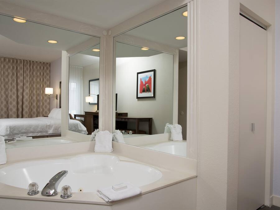 Une salle de bain d’hôtel avec un grand miroir, une baignoire et un lit visible dans le reflet.
