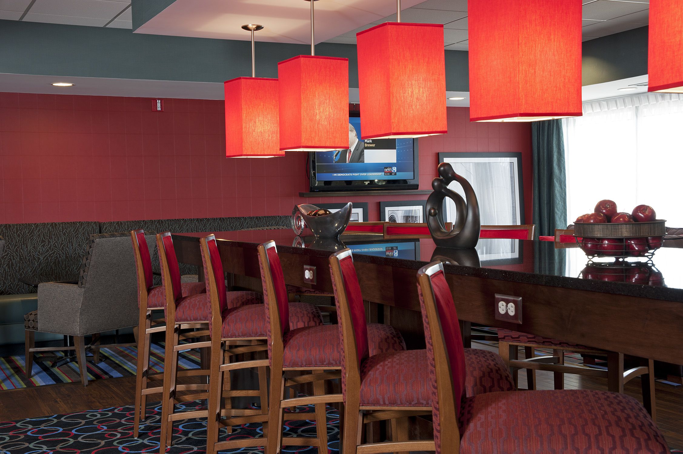 A hotel bar with red chairs, a television, and a red lamp.