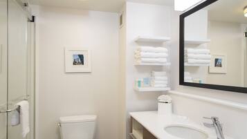 A modern bathroom with a glass shower enclosure, a white toilet, a sink with a mirror, and shelves with folded towels.