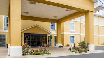 A hotel entrance with a covered walkway, large windows, and flower beds.