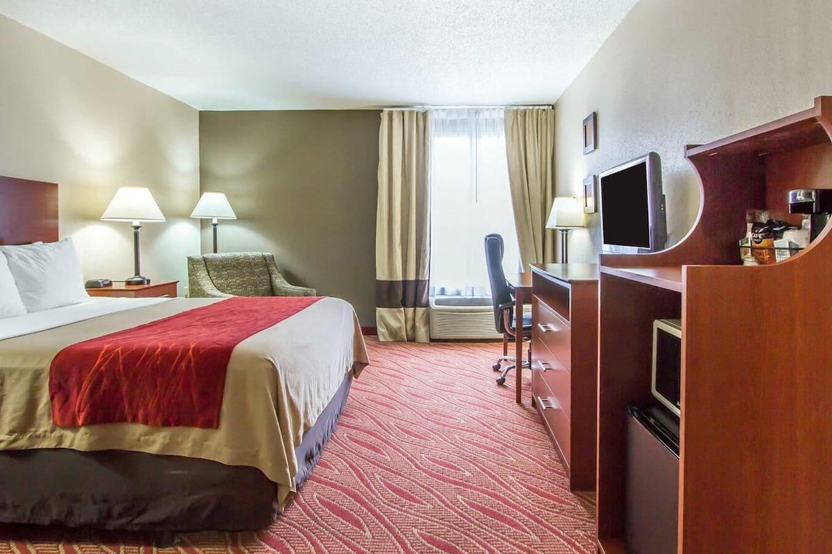 A hotel room with a bed, desk, chair, TV, and a window with curtains.