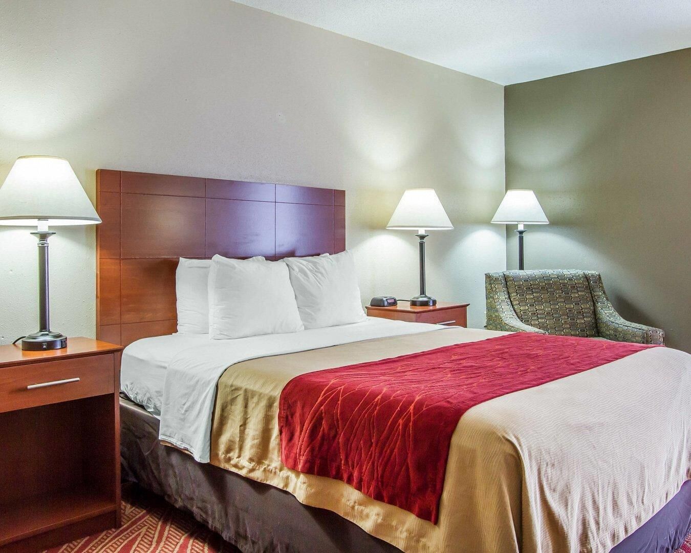 Ein Hotelzimmer mit Bett, zwei Nachttischen, zwei Lampen, einem Sessel und einem Kopfteil.