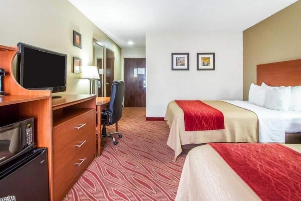 A hotel room with a bed, a desk with a computer, a chair, a microwave, and a television.