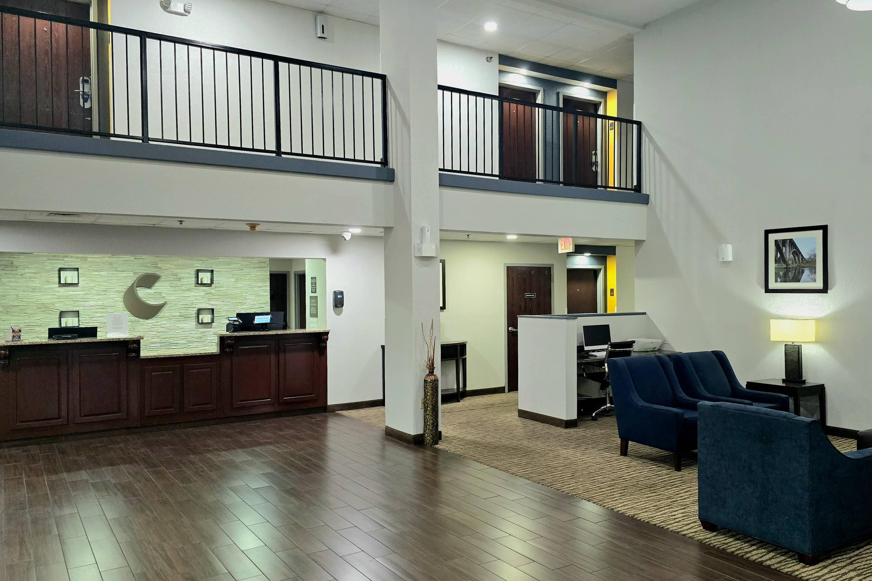 A hotel lobby with a reception desk, seating area, and a staircase to the upper floor.