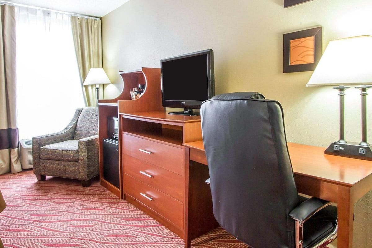 A hotel room with a desk, a chair, a television, and a lamp.