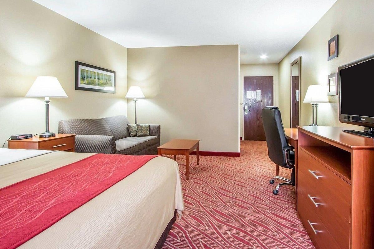 A hotel room with a bed, a desk, a chair, a television, and a lamp.