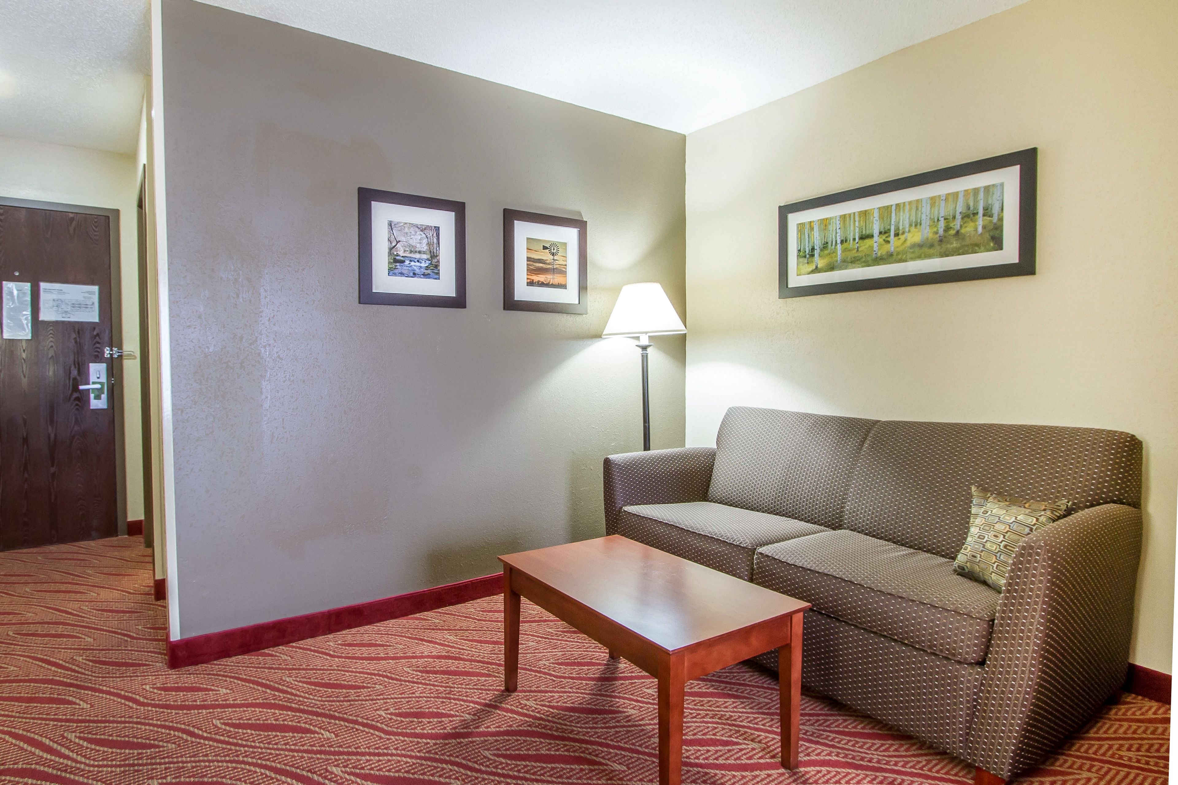 A hotel room with a brown sofa, a small wooden table, a lamp, and two framed pictures on the wall.