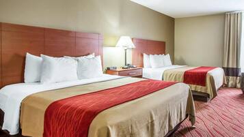 A hotel room with two beds, a nightstand, a lamp, and a window with curtains.