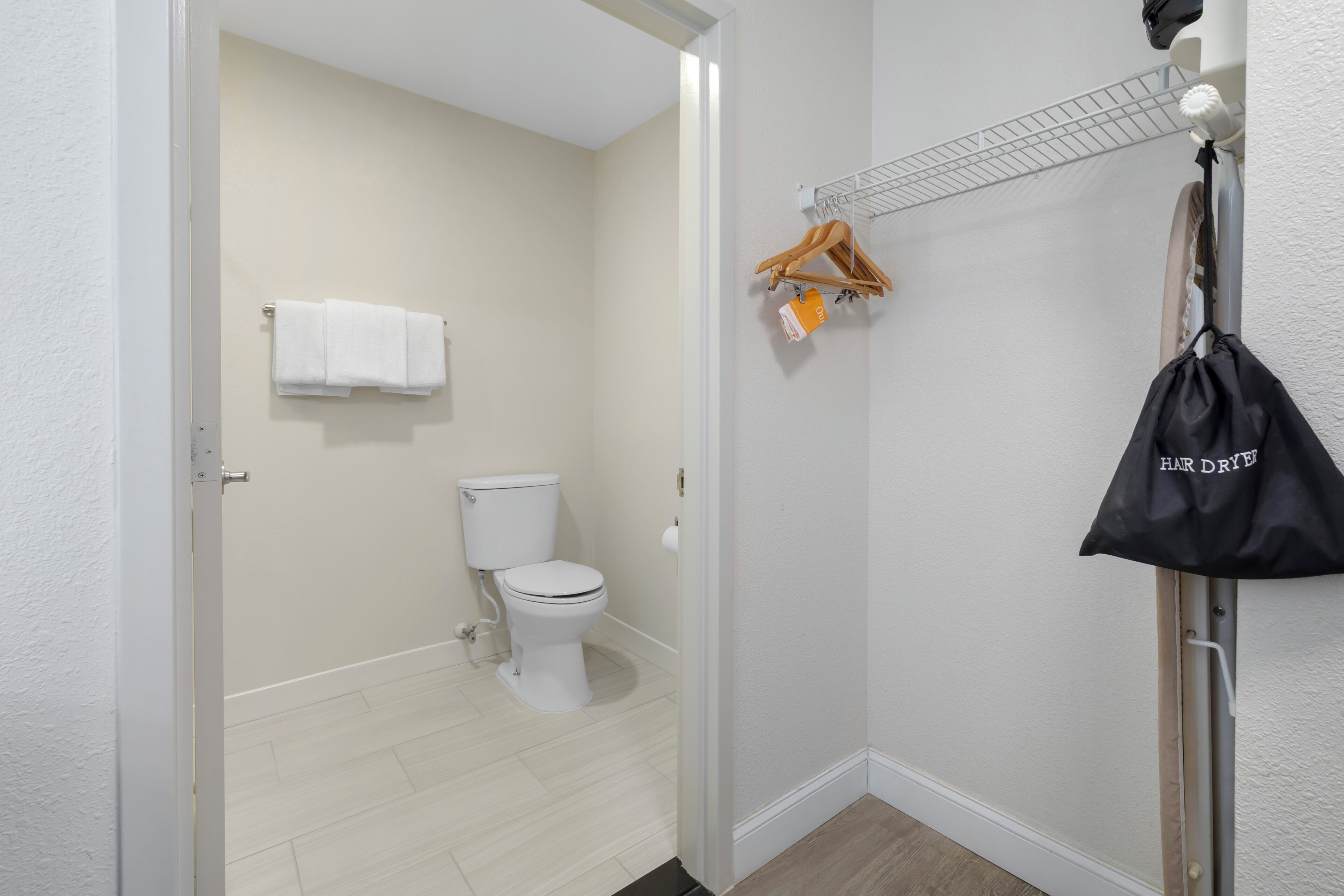 A bathroom with a toilet, a towel rack with towels, a hair dryer, and a bag labeled 'Hair Dryer.'
