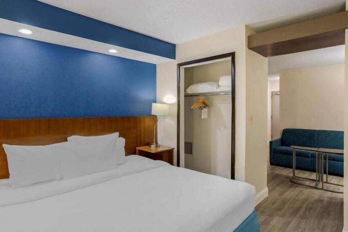 A hotel room with a large bed, a wooden headboard, a nightstand, a desk, and a blue sofa.