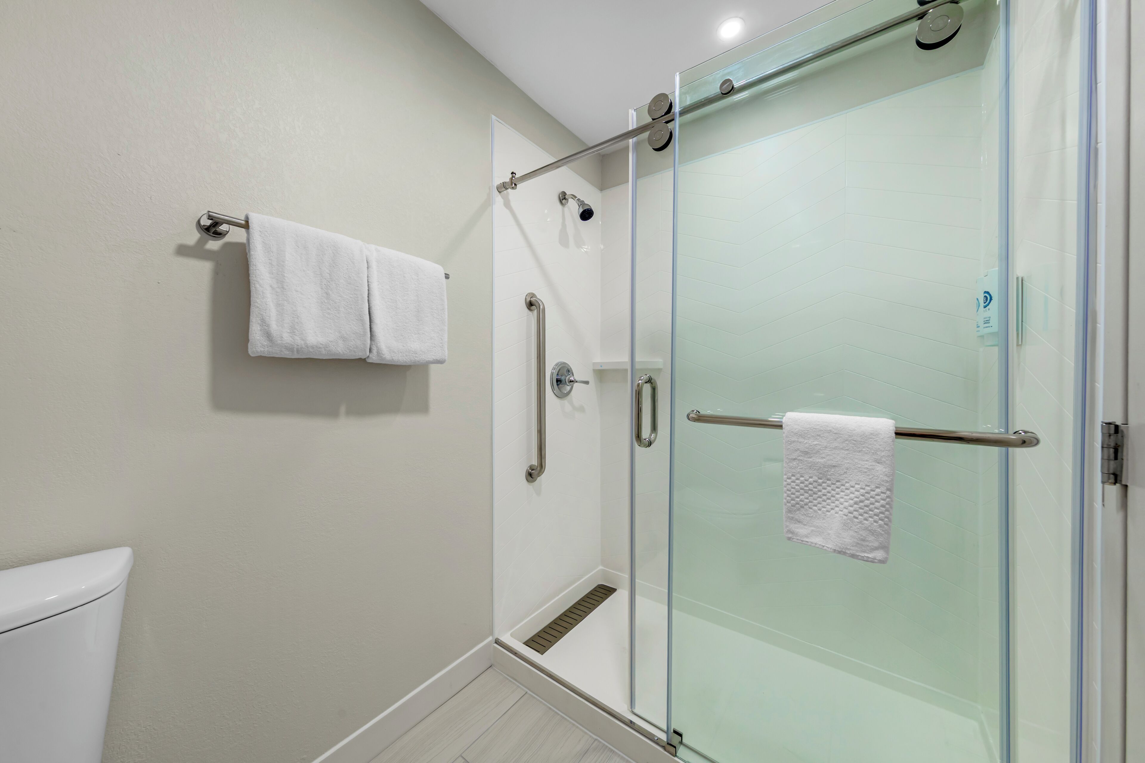Een moderne badkamer met een douchecabine van glas, een witte handdoek op een rek en een toilet.