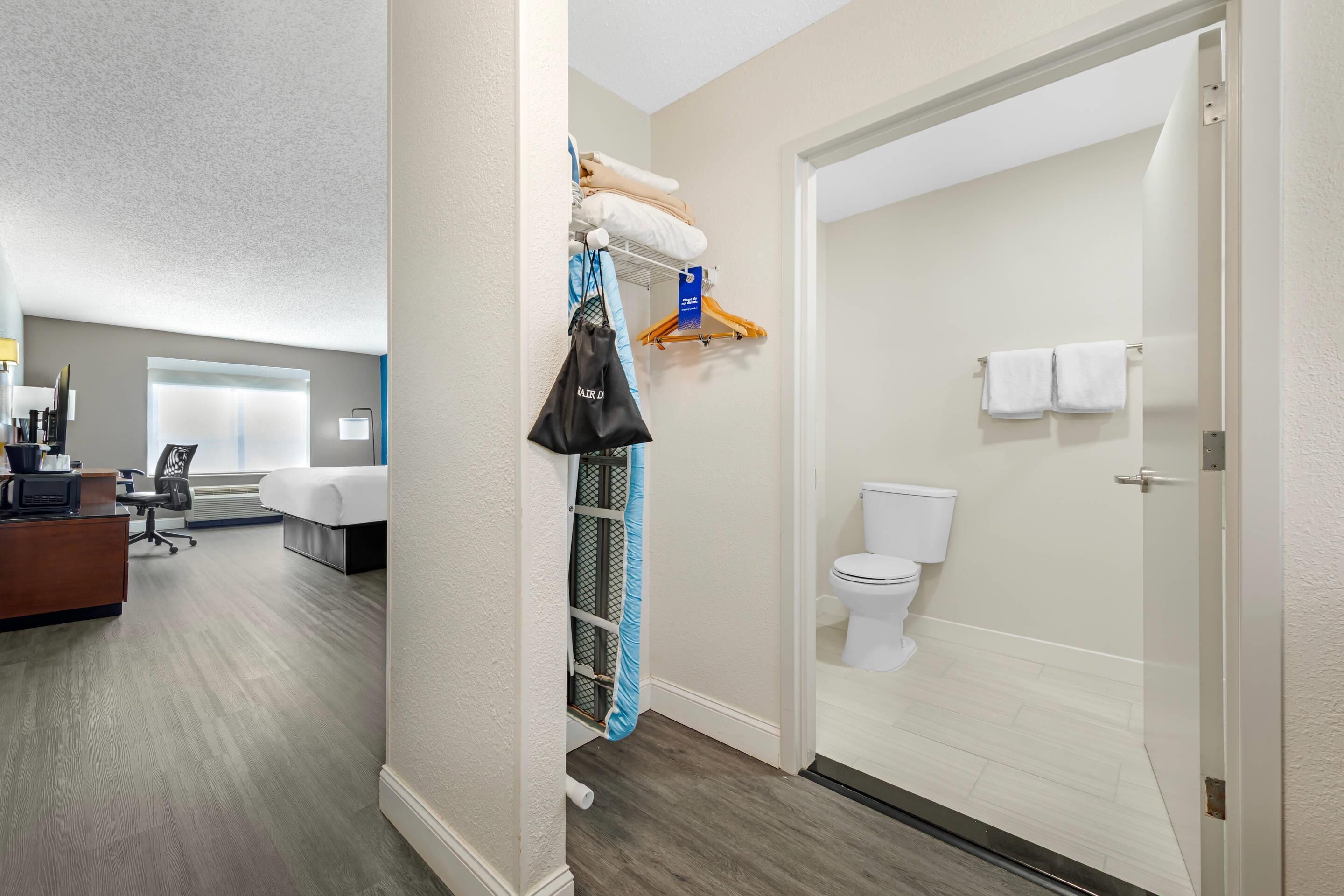 A hotel room with a desk, chair, bed, and a bathroom with a toilet and towel rack.