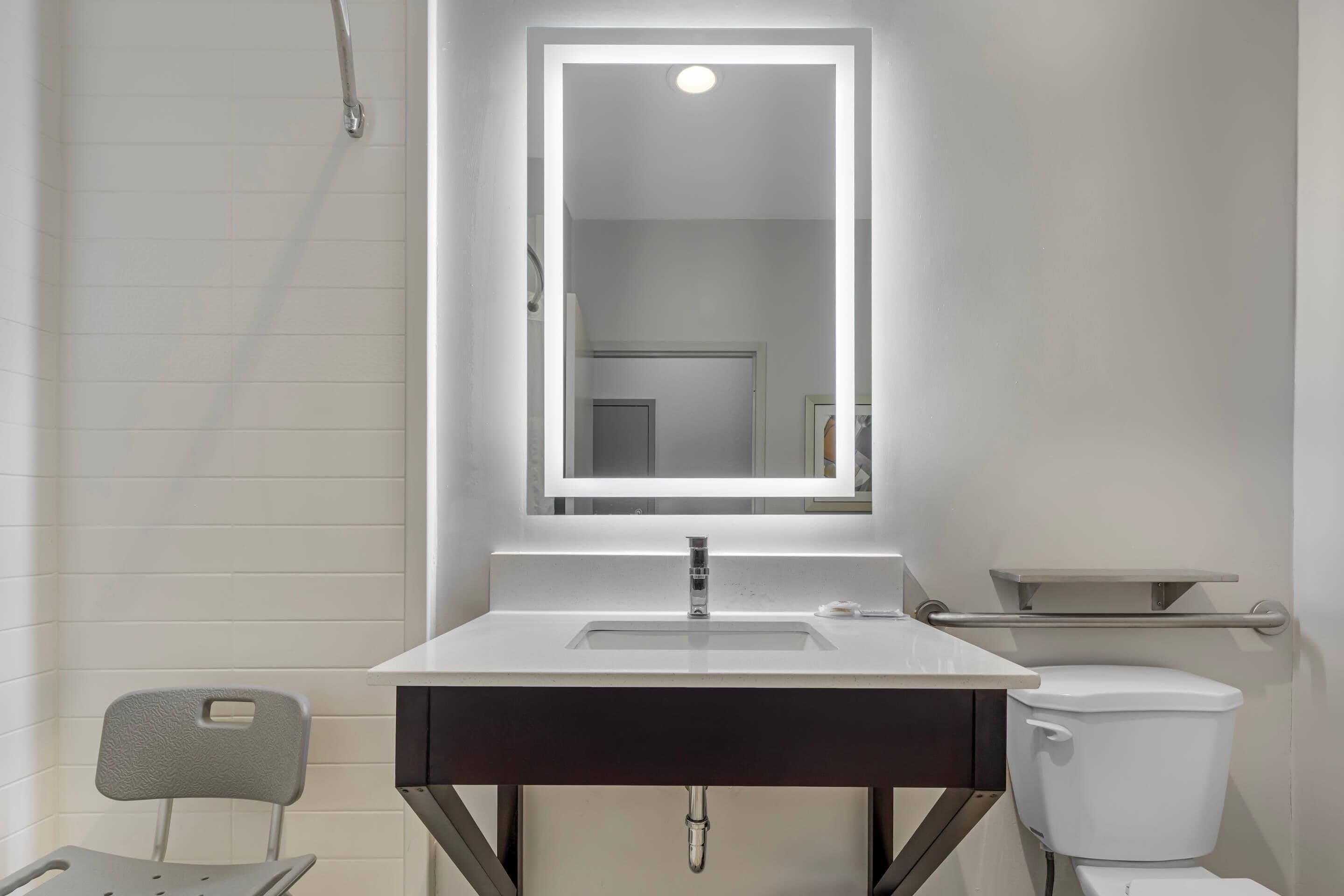 A modern bathroom with a white sink, a mirror with integrated lighting, a toilet, and a showerhead.