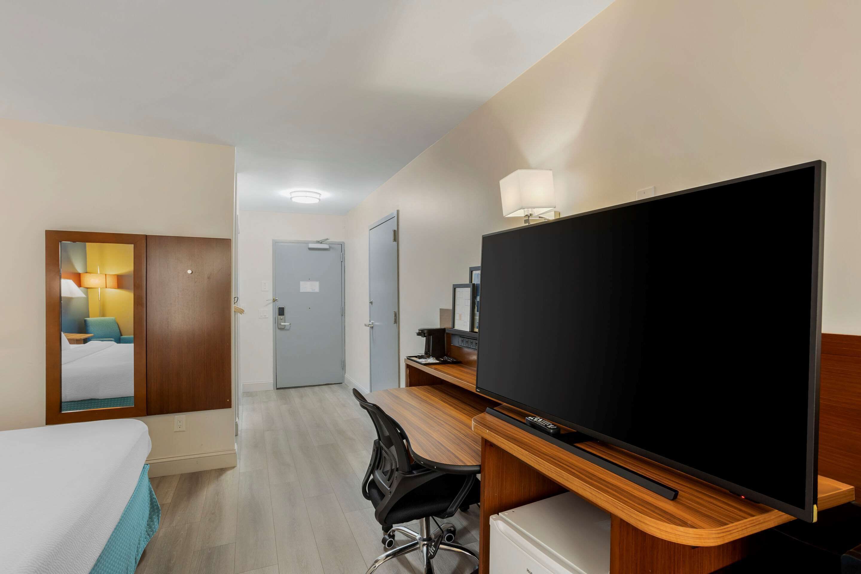 Una habitación de hotel con una cama, un escritorio con computadora, televisor y armario.