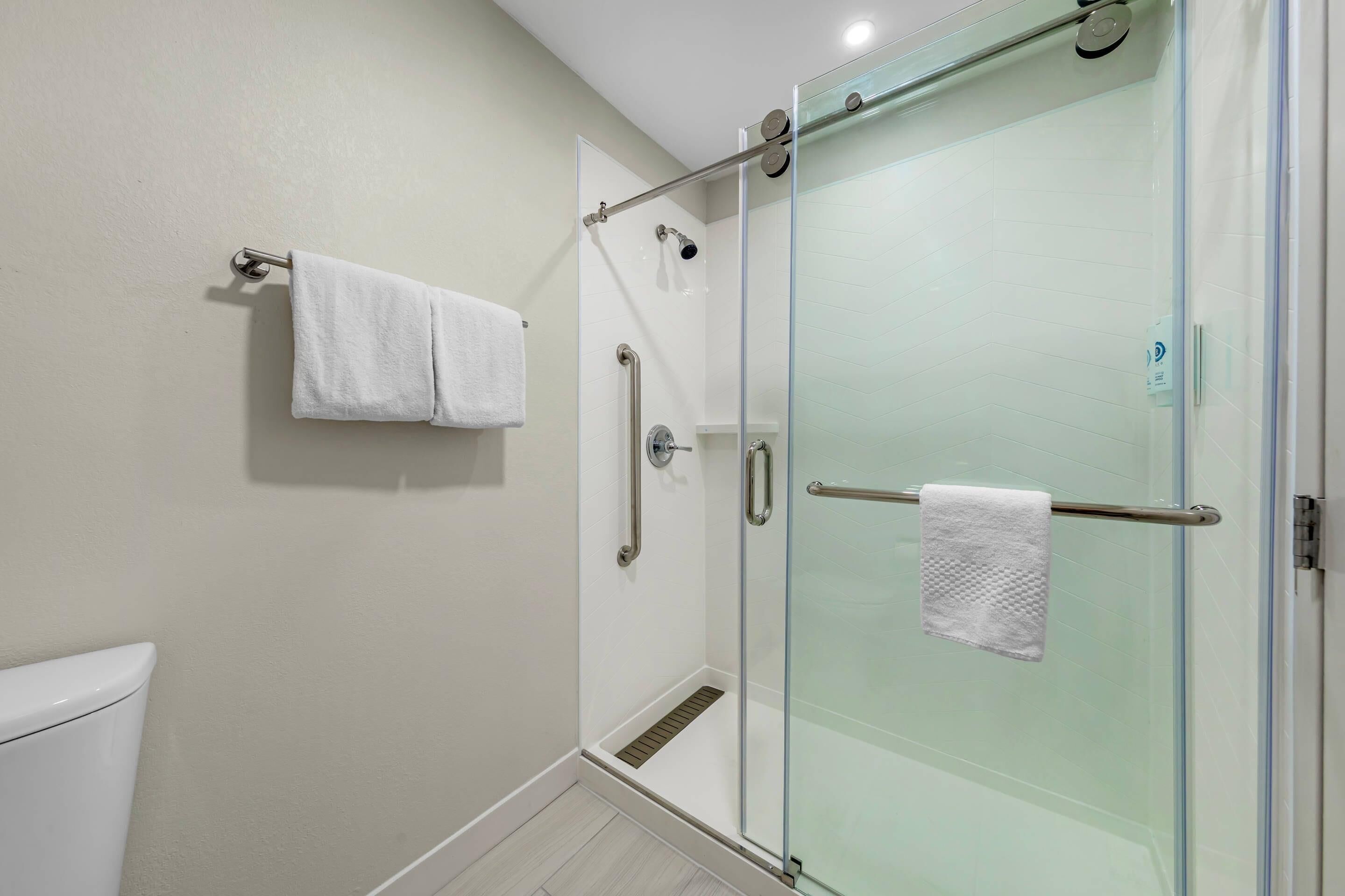 A glass-enclosed shower with a handrail, a white towel on a rack, and a toilet visible to the left.