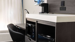 Une chambre d’hôtel compacte équipée d’une kitchenette, d’une machine à café, d’un réfrigérateur et d’une chaise noire.