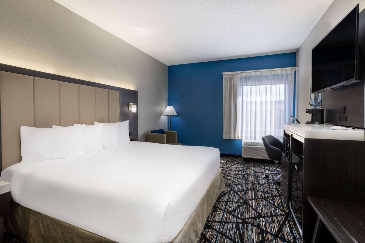 Una habitación de hotel con una cama grande, un escritorio con silla, televisión y ventana con cortinas.