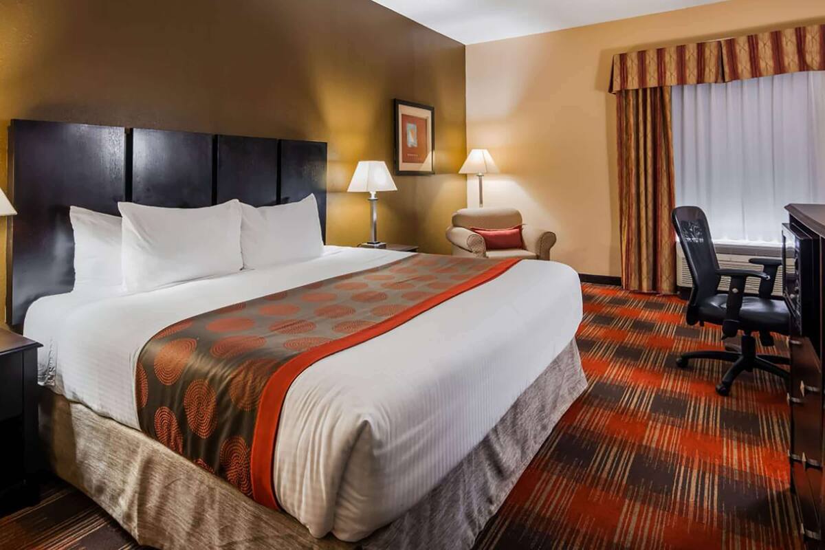 Habitación de hotel con una cama grande, dos mesitas de noche, un escritorio, una silla y una ventana con cortinas.
