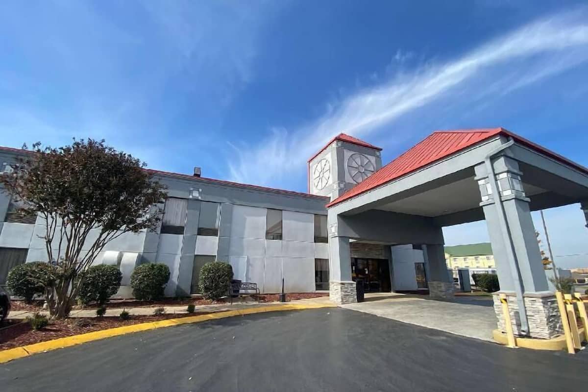 Un edificio con un acceso cubierto, una torre del reloj y un estacionamiento.