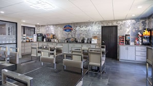 Un espace moderne dédié au petit-déjeuner, avec des sièges, un coin café et un comptoir où sont présentés divers aliments.