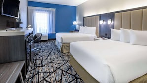 Une chambre d’hôtel avec deux lits, un bureau, une télévision et une fenêtre avec des rideaux.