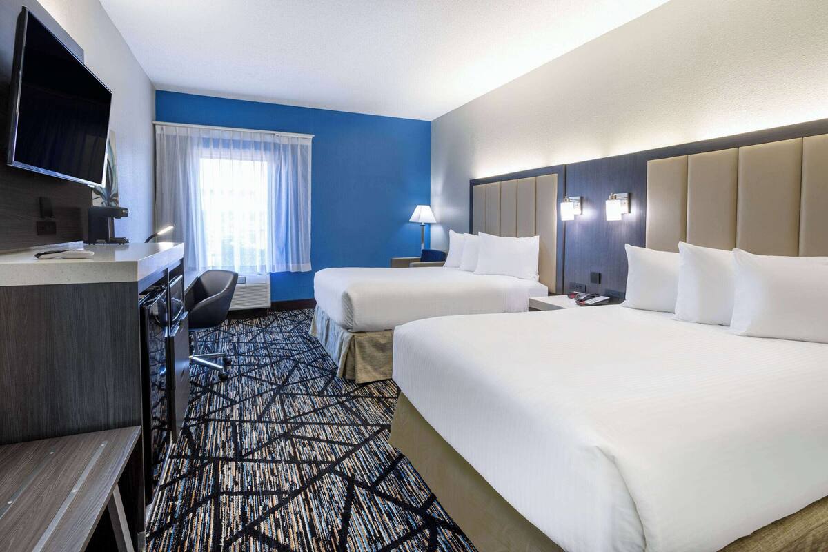 Habitación de hotel con dos camas, un escritorio, un televisor y una ventana con cortinas.