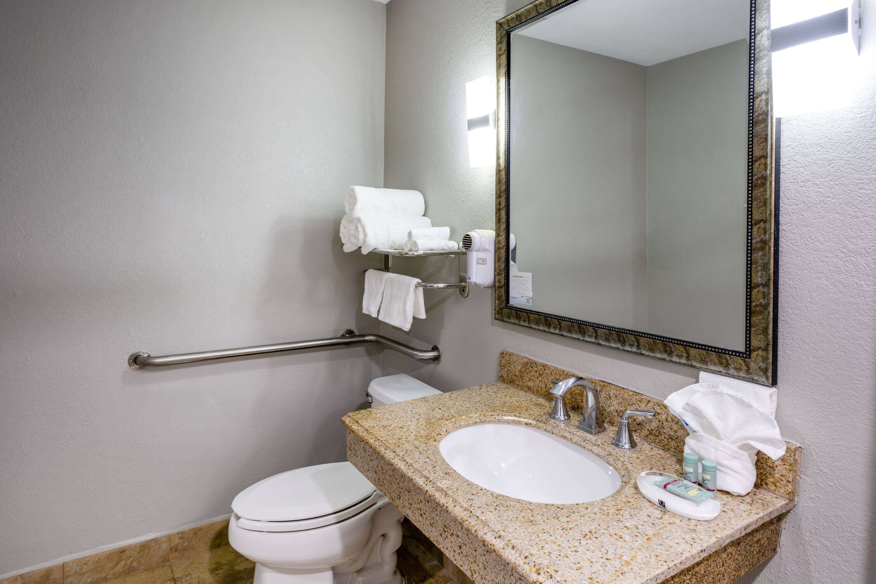 A bathroom with a white toilet, a granite countertop sink, a mirror, and a grab bar.