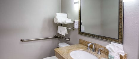 A bathroom with a white toilet, a granite countertop sink, a mirror, and a grab bar.