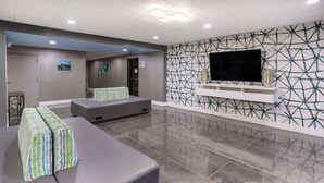 Un hall d’entrée moderne avec un canapé gris, un téléviseur à écran plat fixé sur un mur orné d’un motif géométrique, et un comptoir d’accueil.