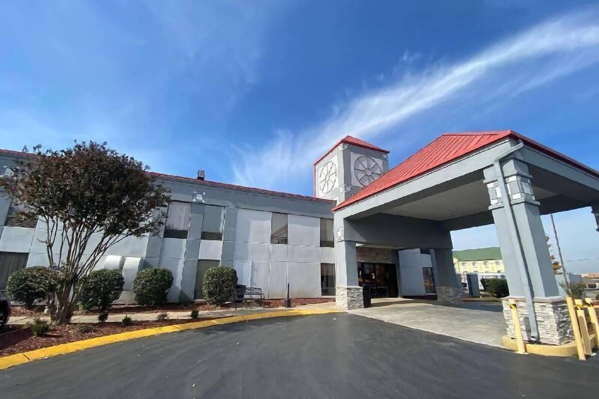Un edificio con un acceso cubierto, una torre del reloj y un estacionamiento.