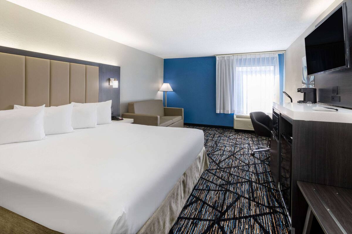 Habitación de hotel con una cama grande, un escritorio, una silla, un televisor y una ventana con cortinas.