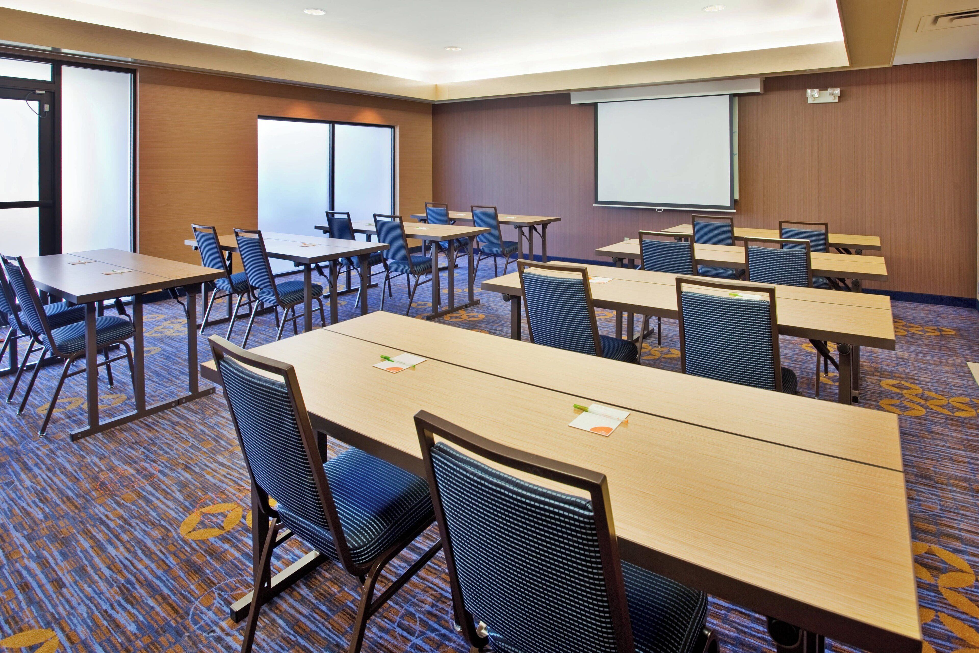 A conference room with multiple tables and chairs, a projector screen, and a carpeted floor.