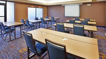 A conference room with multiple tables and chairs, a projector screen, and a carpeted floor.
