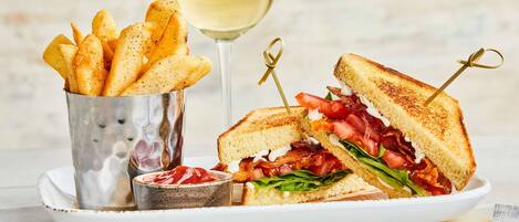A plate with a grilled sandwich, a glass of white wine, and a container of fries.
