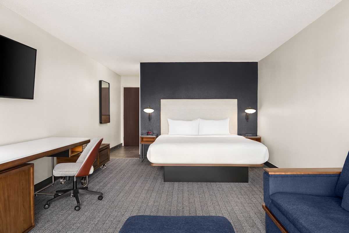 A hotel room with a large bed, a desk with a chair, a sofa, and two bedside lamps.
