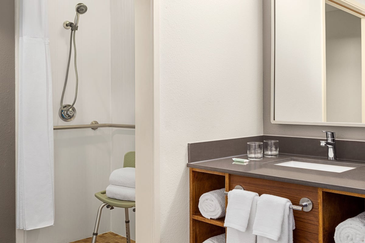 A bathroom with a shower, a sink, and a mirror. There are towels and glasses on the counter.