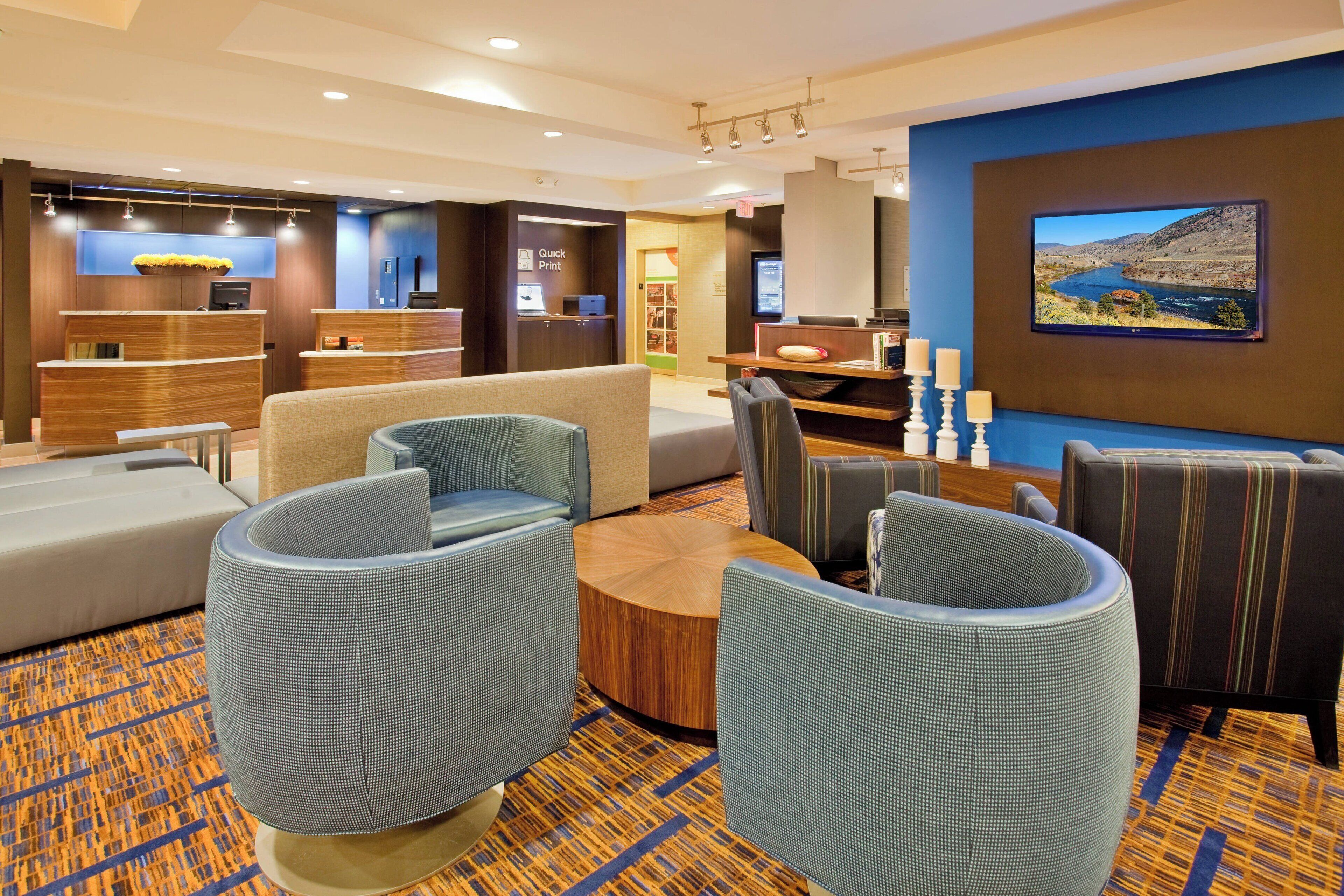Un hall de hotel con zonas de estar, un mostrador de recepción y una pantalla grande que muestra un paisaje pintoresco.