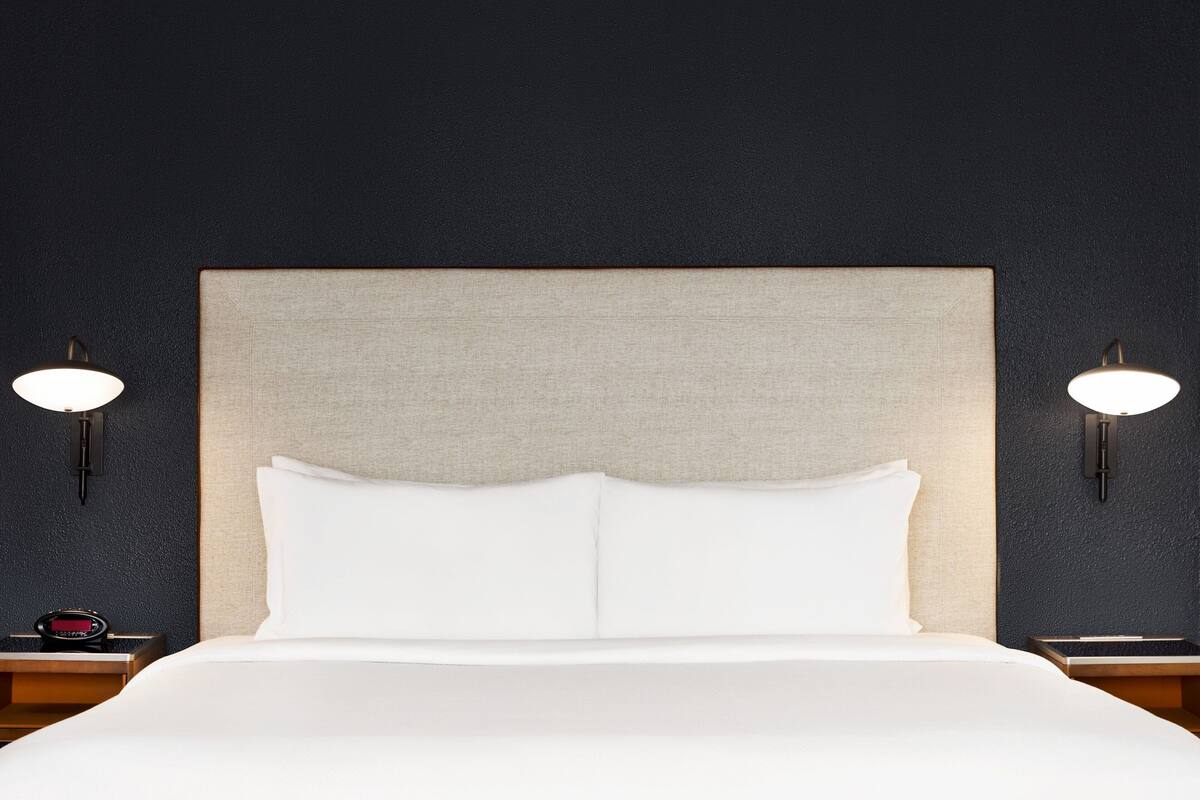 A bed with a beige headboard and white bedding, flanked by two wall-mounted nightstands with lamps.