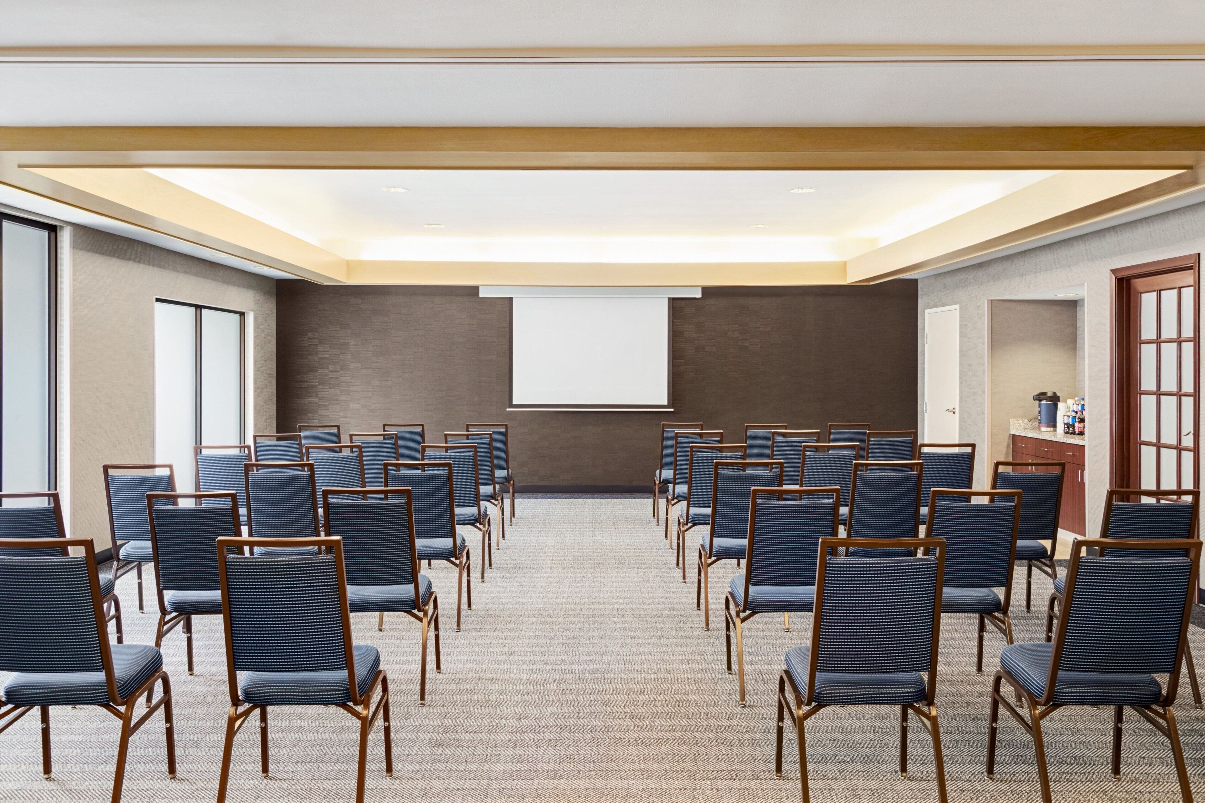 A conference room with rows of chairs facing a projection screen, carpeted floor, and a wooden ceiling.