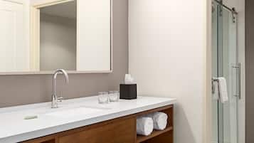 A modern bathroom with a large mirror, a white sink, a glass shower enclosure, and wooden shelves with towels.