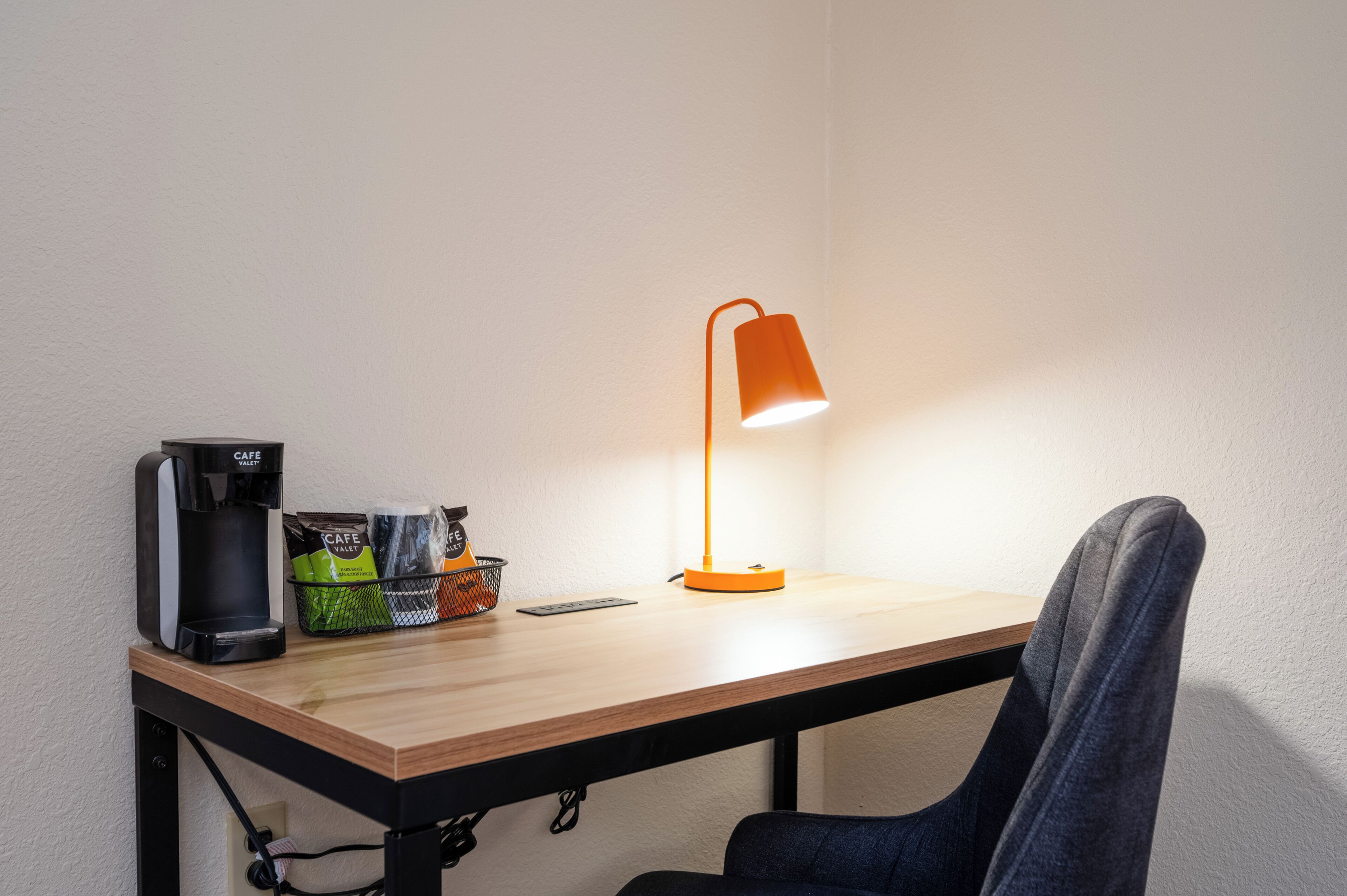 A small table with a coffee maker, a basket of snacks, and a desk lamp.