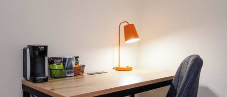 A small table with a coffee maker, a basket of snacks, and a desk lamp.
