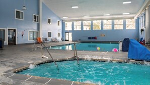Una piscina interior con agua cristalina, un trampolín y una sala iluminada con ventanas.