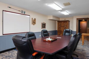 Una sala de conferencias con una mesa grande, cuatro sillas de cuero negro, una pizarra y un armario de madera.