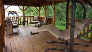 Una terraza techada al aire libre con piso de madera, sillas acolchadas y una hamaca.