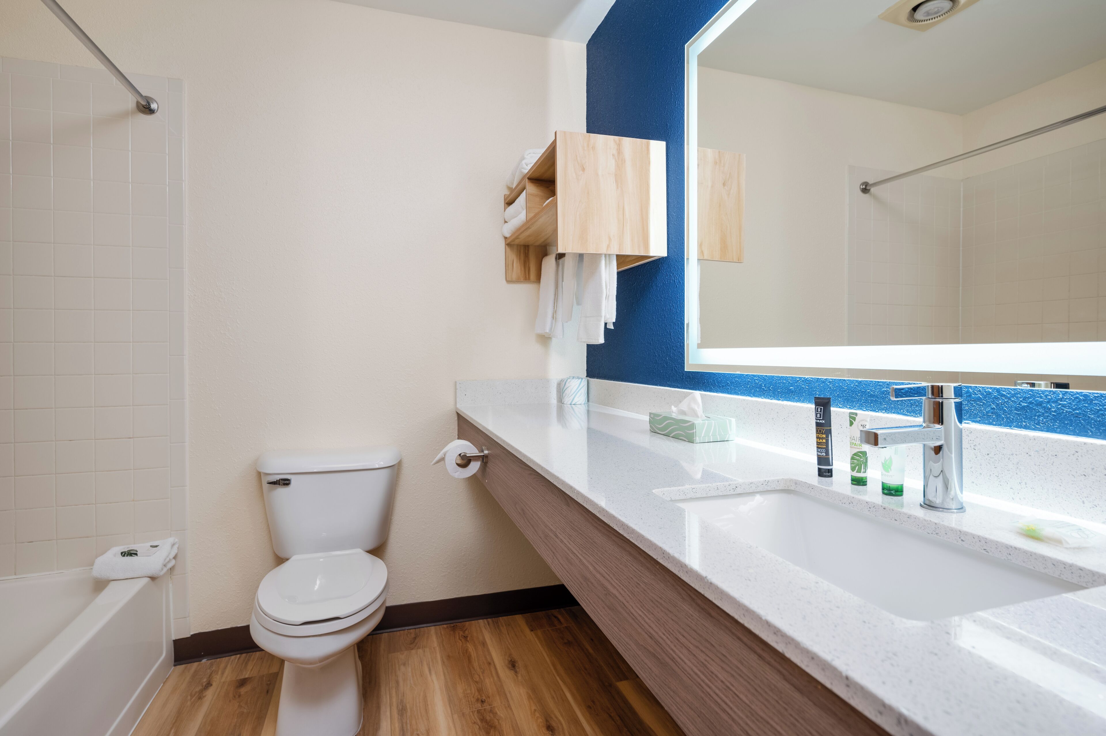 A bathroom with a toilet, sink, mirror, and wooden shelf with towels.